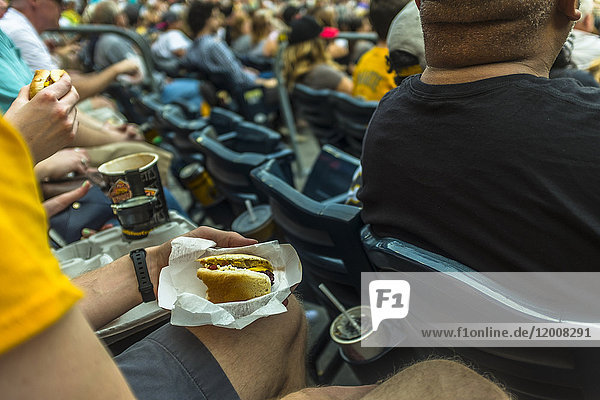 Mann sitzt im Stadion und isst Hot Dog