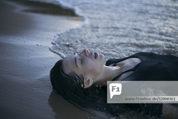 Kaukasische Frau liegt am Strand in den Wellen