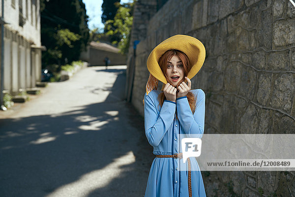 Überraschte kaukasische Frau mit Hut in der Nähe einer Steinmauer