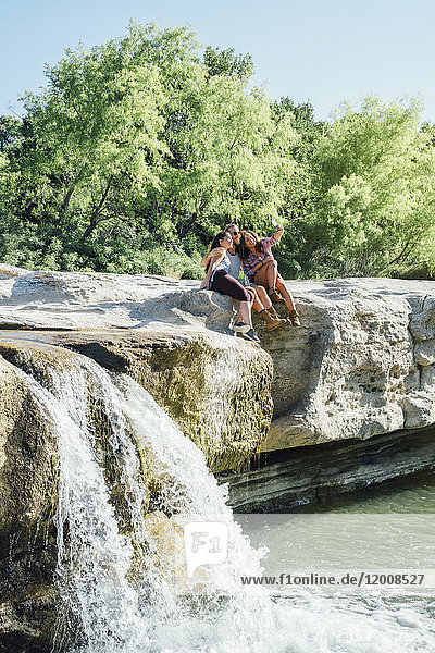 Freunde posieren für ein Handy-Selfie auf Felsen in der Nähe eines Wasserfalls