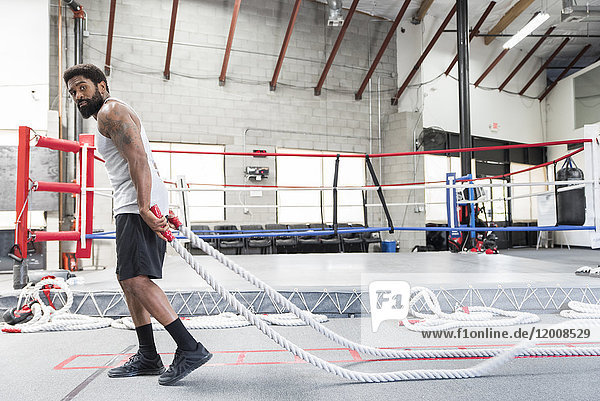 Black man pulling heavy ropes in gymnasium