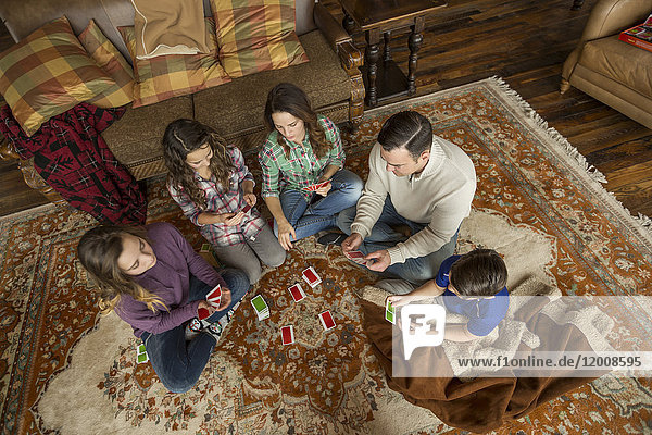 Kaukasische Familie sitzt auf einem Teppich und spielt ein Kartenspiel