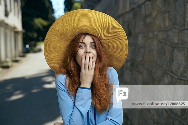 Surprised Caucasian woman wearing hat near stone wall