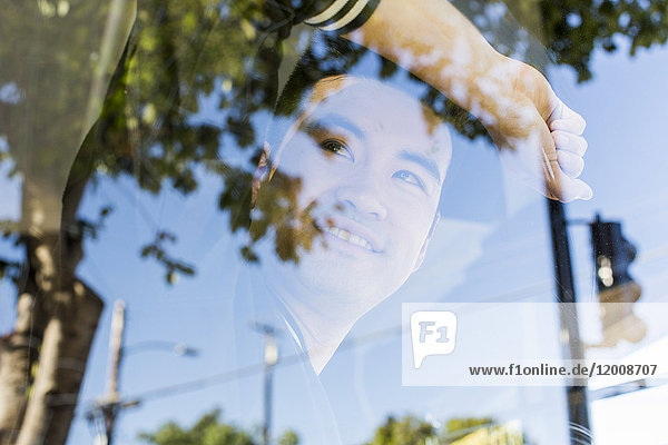 Lächelnder chinesischer Mann lehnt sich an ein Fenster