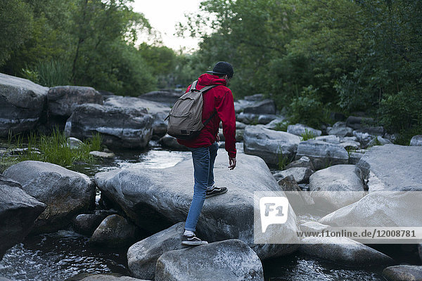 Kaukasischer Mann wandert auf Felsen im Fluss