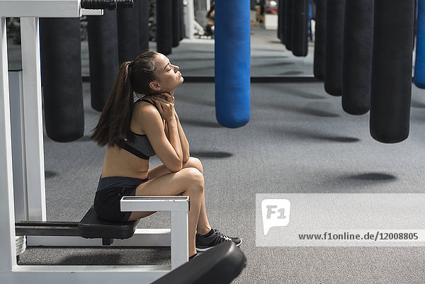 Mixed race woman sitting in gymnasium rubbing neck