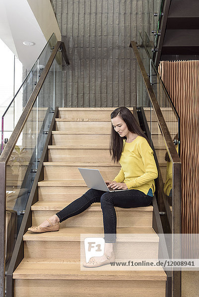 Gemischtrassige Frau sitzt auf einer Treppe und benutzt einen Laptop