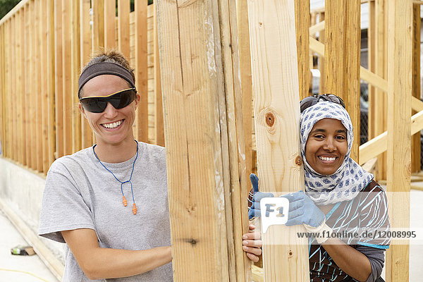 Smiling volunteers holding lumber at construction site
