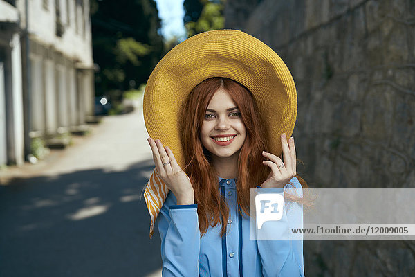 Lächelnde kaukasische Frau mit Hut in der Nähe einer Steinmauer