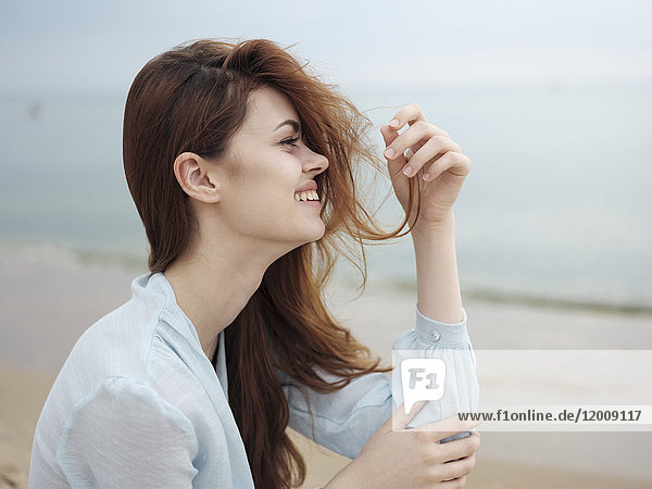 Lächelnde Frau mit Haaren am Strand sitzend