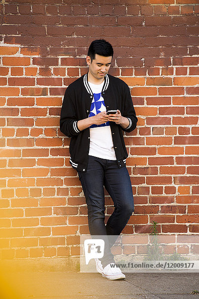 Chinese man leaning on brick wall texting on cell phone