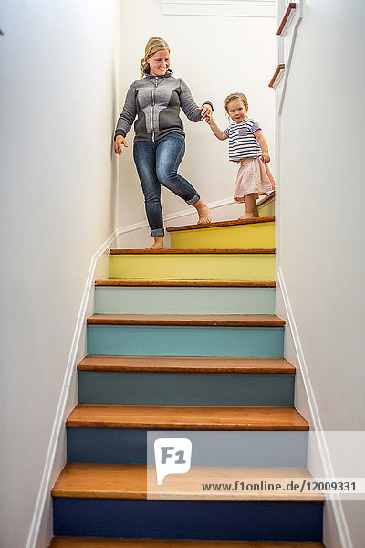 Kaukasische Mutter und Tochter steigen eine mehrfarbige Treppe hinunter