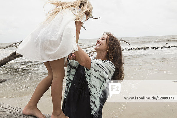 Caucasian mother and daughter playing on driftwood on beach
