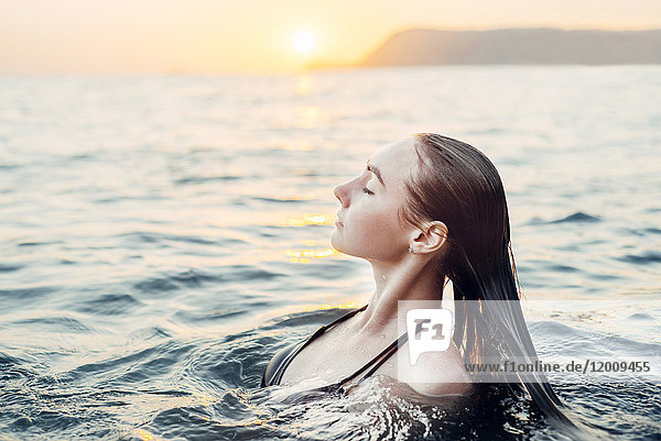 Kaukasische Frau beim Schwimmen im Sonnenuntergang