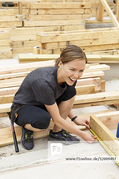 Lächelnde kaukasische Frau misst Holz auf einer Baustelle