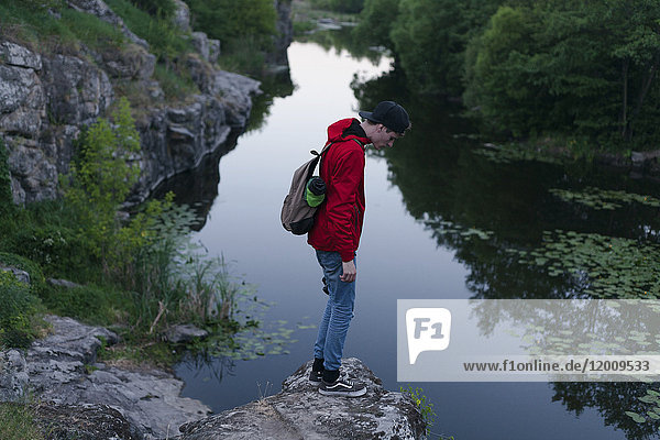 Kaukasischer Mann steht auf einem Felsen und schaut auf den Fluss hinunter