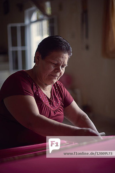 Hispanic woman weaving fabric on loom