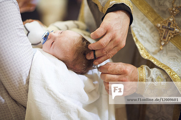 Priester schneidet die Haare eines kleinen Mädchens