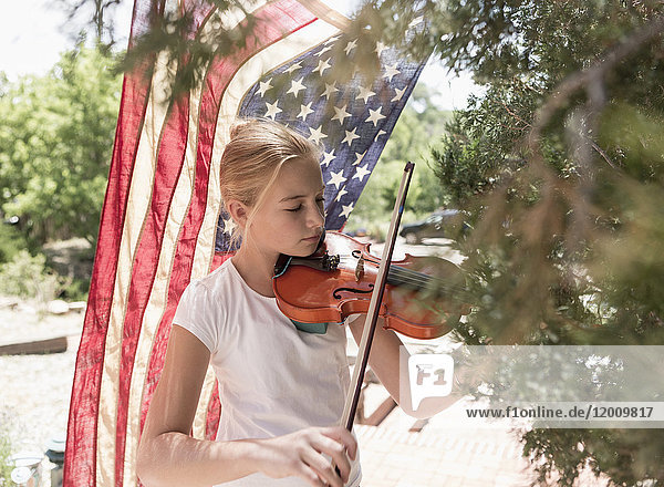 Kaukasisches Mädchen spielt Geige in der Nähe der amerikanischen Flagge