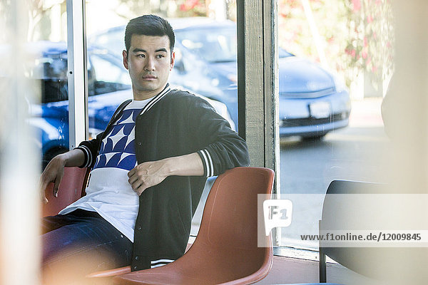 Ernster chinesischer Mann sitzt auf einem Stuhl am Fenster
