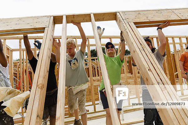 Volunteers lifting framed wall at construction site