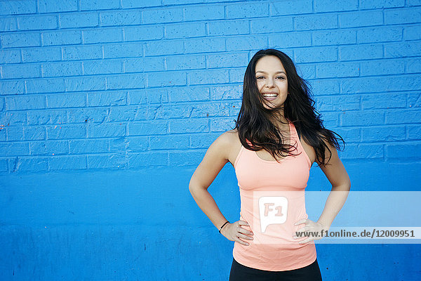 Wind blowing hair of smiling mixed race woman at blue wall
