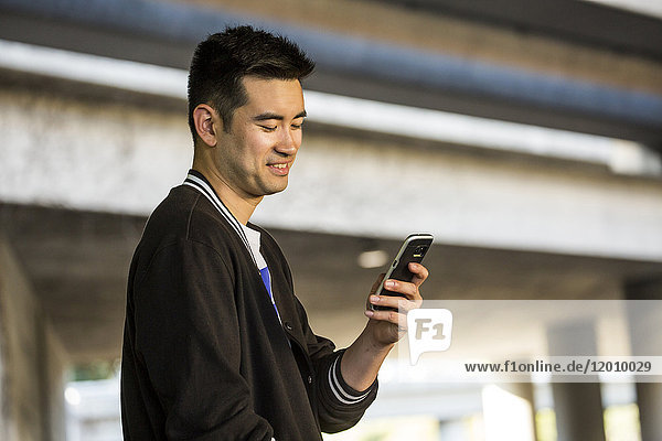 Lächelnder chinesischer Mann  der eine SMS auf seinem Mobiltelefon schreibt