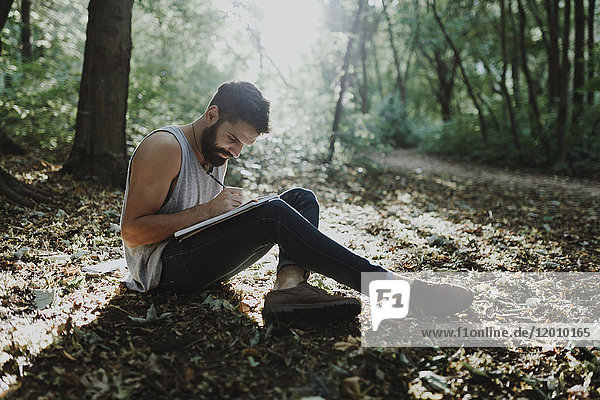 Caucasian man sitting in woods drawing on sketchpad