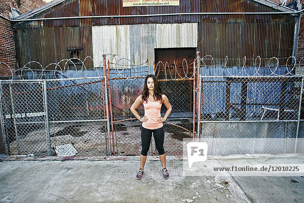 Confident mixed race woman standing on sidewalk near barbed-wire fence