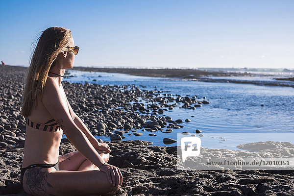 Caucasian woman sitting on beach wearing bikini