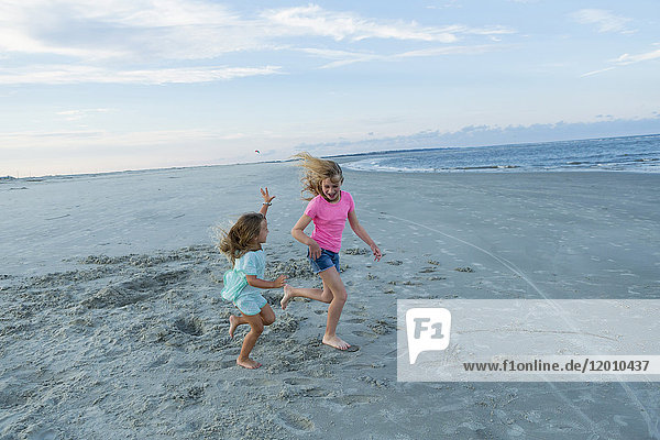 Caucasian sisters running on windy beach