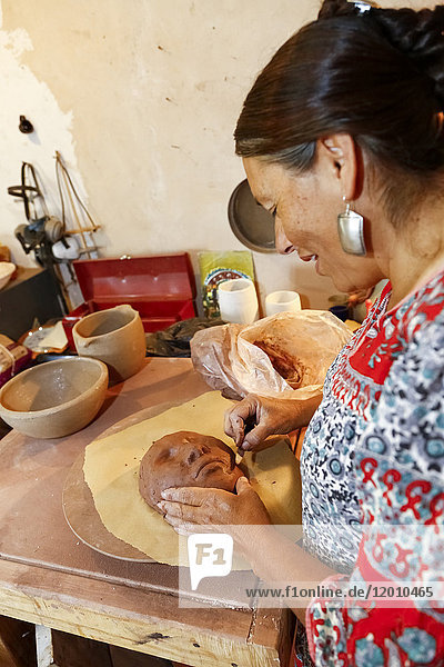 Mixed race woman shaping clay mask in art studio