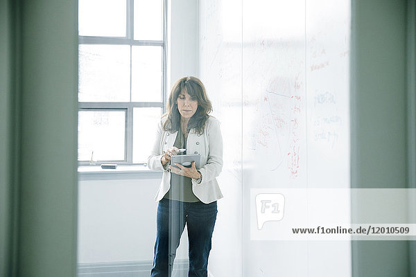 Kaukasische Geschäftsfrau hält digitales Tablet in der Nähe von Whiteboard