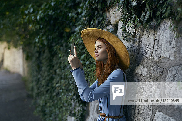 Kaukasische Frau fotografiert mit Handy in der Nähe einer Steinmauer