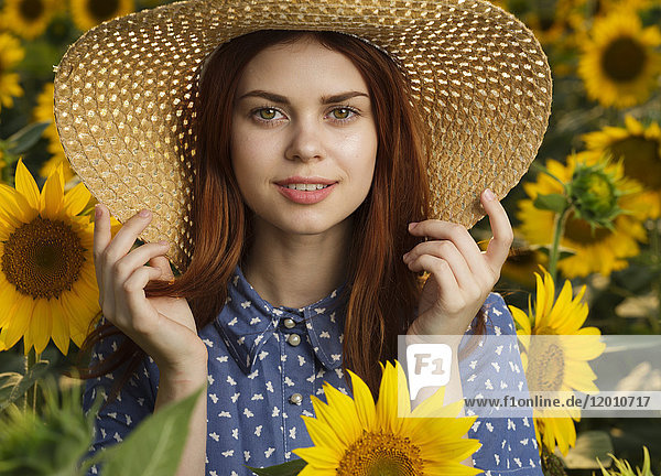 Lächelnde kaukasische Frau mit Hut in einem Sonnenblumenfeld