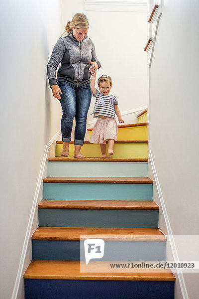 Kaukasische Mutter und Tochter steigen eine mehrfarbige Treppe hinunter