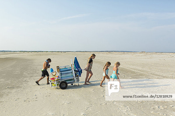 Caucasian boy and girls pulling cart on beach