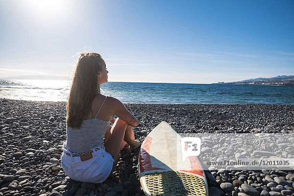 Kaukasische Frau sitzt am Strand in der Nähe von Surfbrett