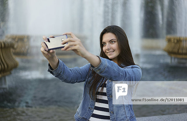 Kaukasische Frau posiert für Handy-Selfie in der Nähe des Brunnens