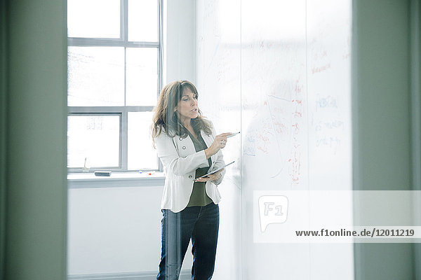 Caucasian businesswoman holding digital tablet and writing on whiteboard