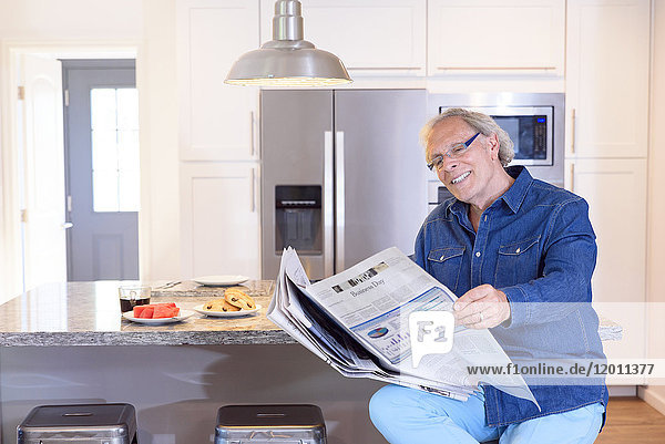 Kaukasischer Mann liest in der Küche Zeitung