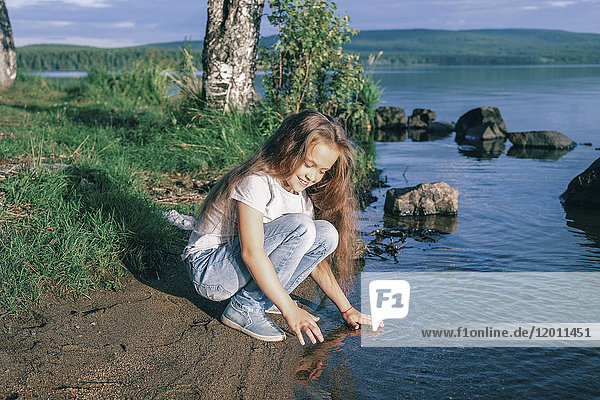 Kaukasisches Mädchen hockt in der Nähe des Flusses