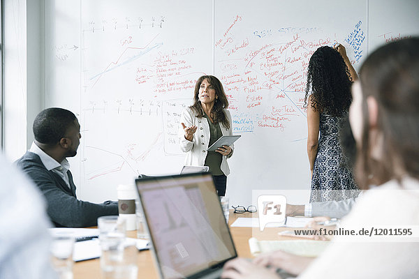Geschäftsfrau hält digitales Tablet in der Nähe des Whiteboards in einer Besprechung