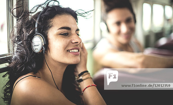 Two young people sitting on a bus wearing headphones.