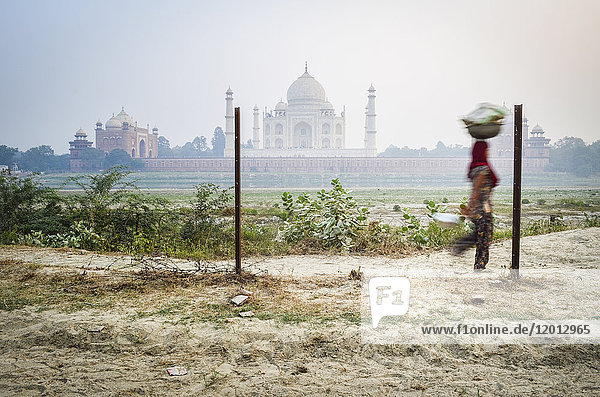 Exterior view of the Taj Mahal in Agra,  India. A woman in the foreground carrying a load on her head.