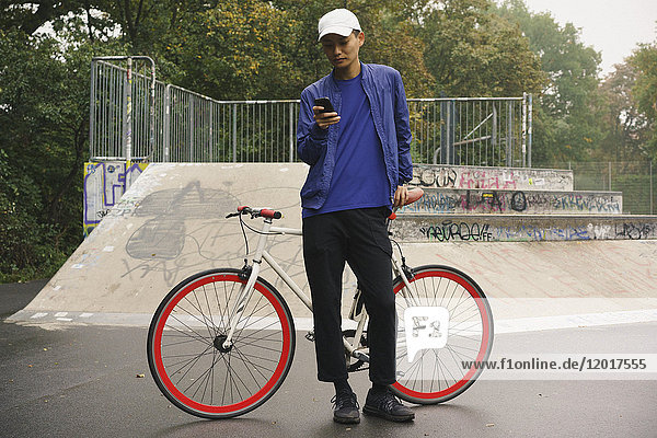 Full length of man using mobile phone while standing with bicycle at park