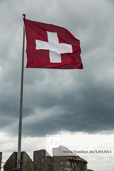 Flachwinkelansicht der Schweizer Fahne bei Wind und bewölktem Himmel