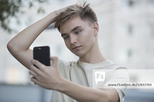 Teenage boy taking selfie from mobile phone with hand in hair