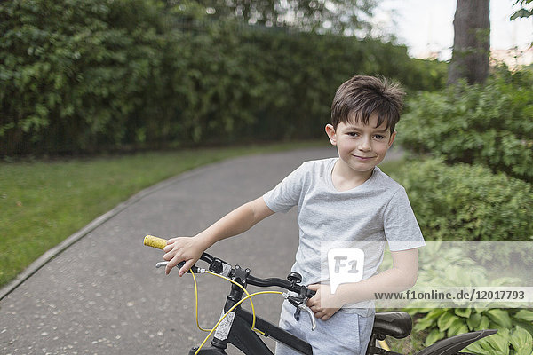 Portrait of boy riding bicycle on street against plants