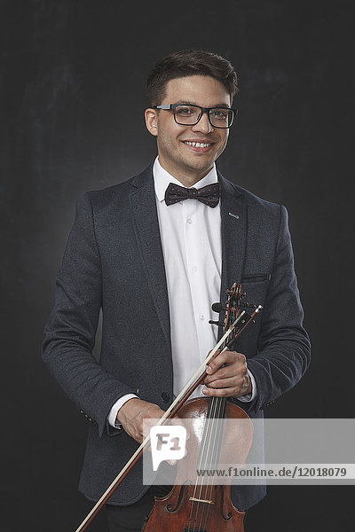 Porträt eines lächelnden jungen Mannes mit Geige auf schwarzem Hintergrund